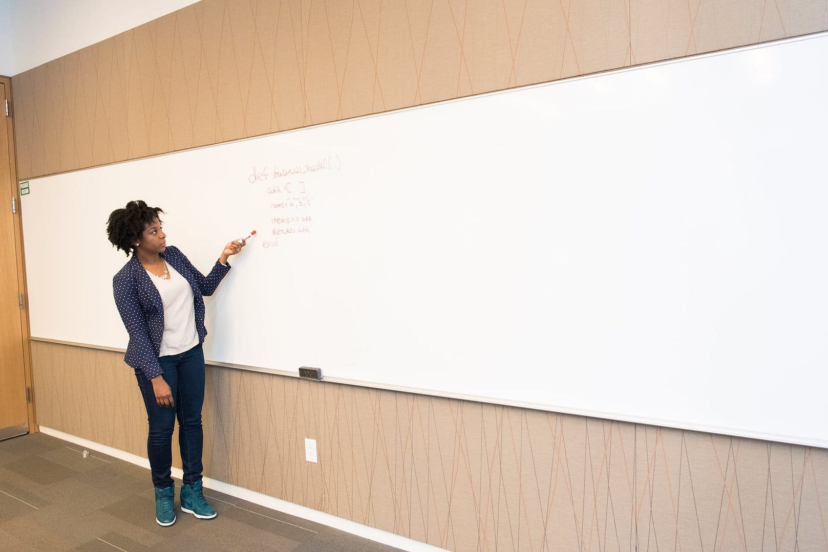 woman wearing black blazer holding pen pointing white marker board